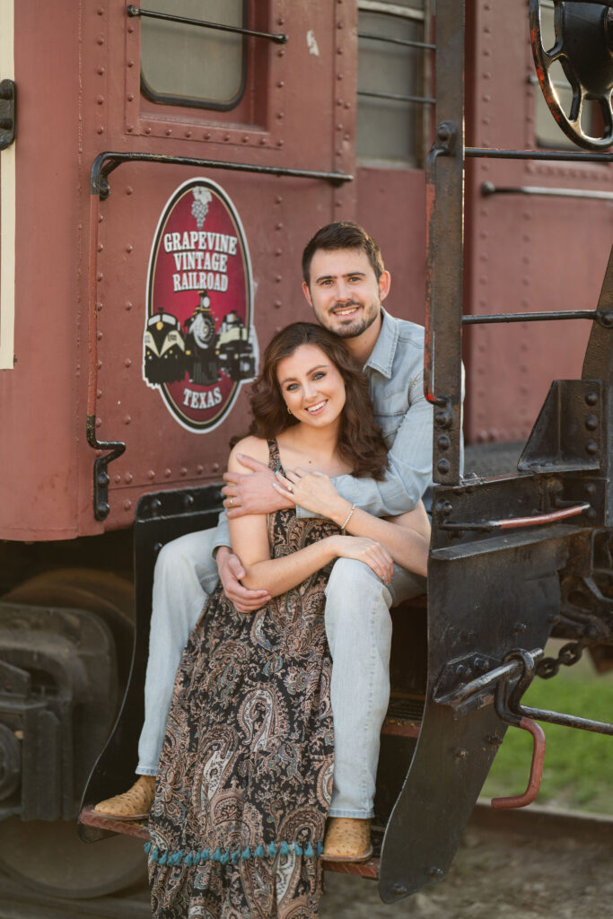 Smiling couple cuddling on a Grapevine Vintage Railroad car during their Stockyards session