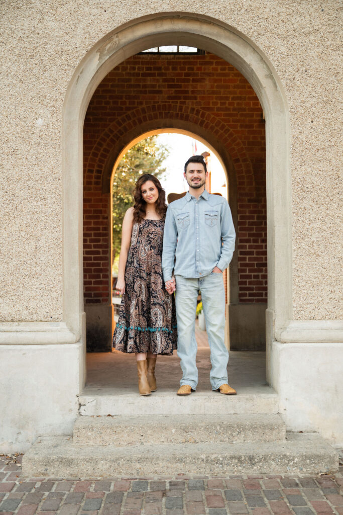 Couple standing hand in hand inside a historic brick archway at the Fort Worth Stockyards