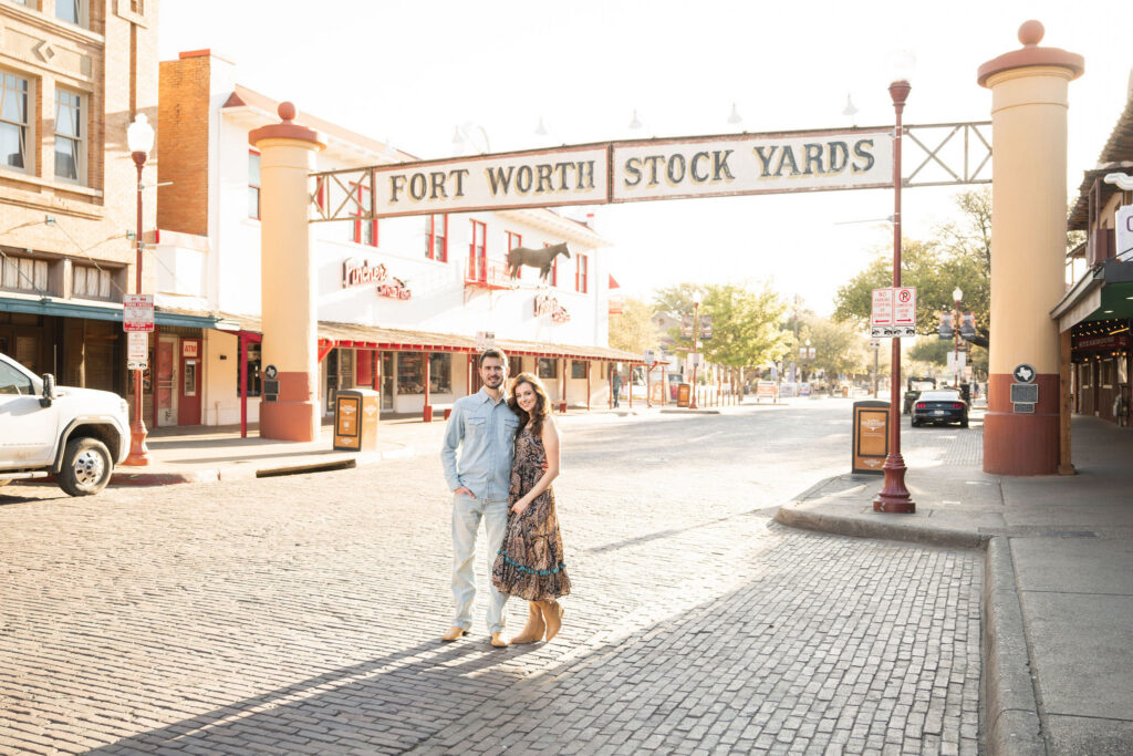 Couple posing beneath the Fort Worth Stock Yards entrance sign during a sunrise photo session
