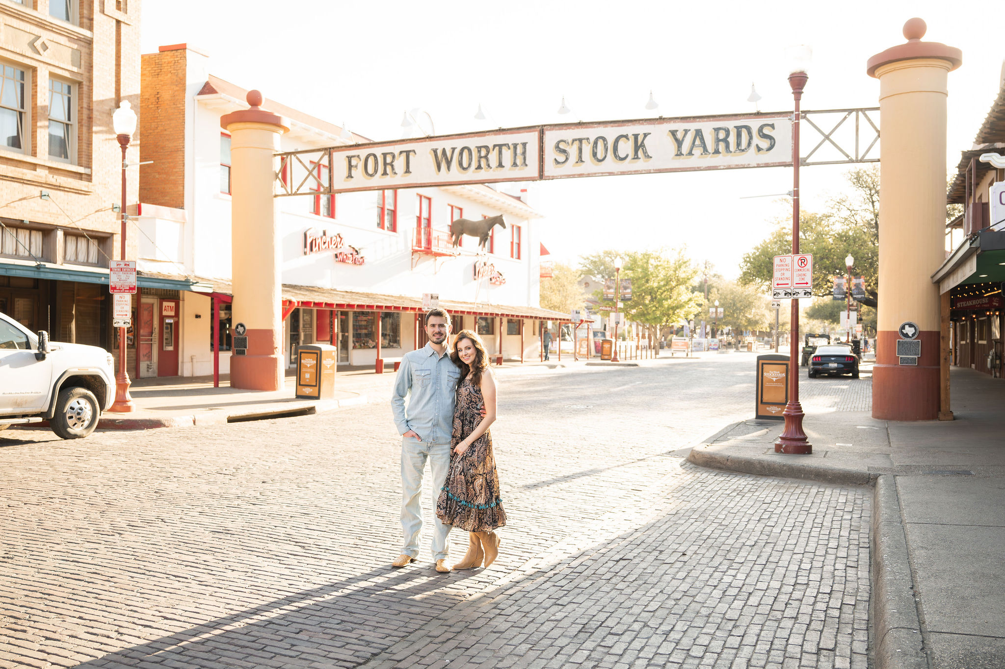 Couple posing beneath the Fort Worth Stock Yards entrance sign during a sunrise photo session