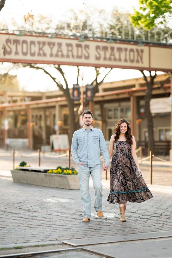 Couple holding hands beneath the Stockyards Station sign at the Fort Worth Stockyards