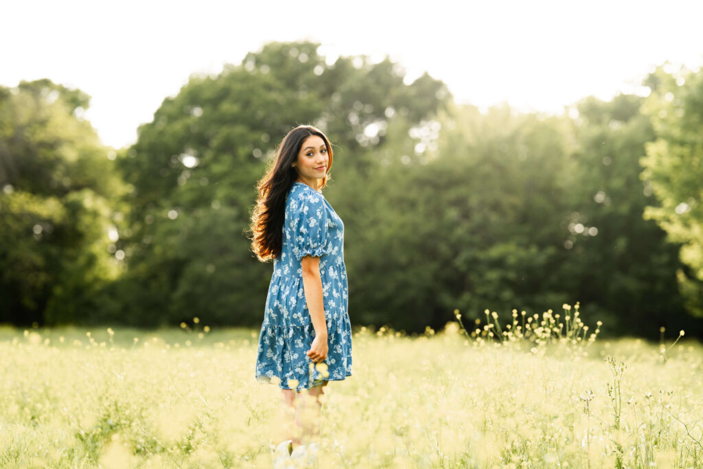 Woman in a blue floral dress standing in a sunlit field during a golden-hour portrait session in Keller, Texas.